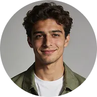 Young man with curly brown hair wearing an olive jacket and white shirt, smiling at the camera.