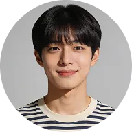 Portrait of a young man with black hair wearing a striped shirt, smiling against a gray background.